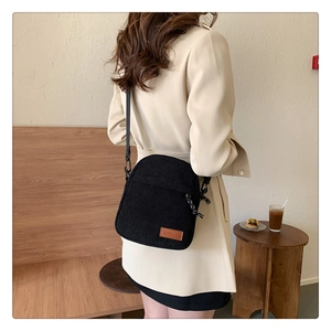 Close-up of black corduroy crossbody bag texture and leather logo on cream coat