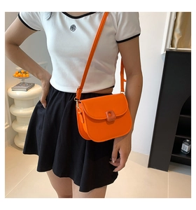 Detail of an orange leather saddle bag with matching square buckle on a model
