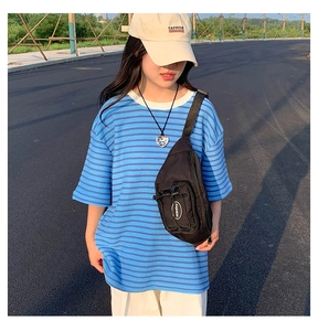 Détail d'un sac banane tactique noir avec écusson de mode sur un t-shirt rayé bleu
