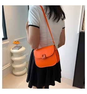 Detailed view of a bright orange saddle bag with resin buckle on a female model
