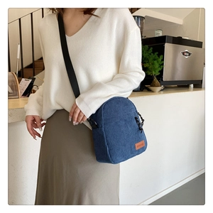 Detail of navy blue corduroy crossbody bag worn by model in a modern cafe setting