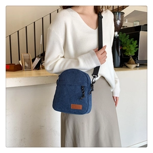 Deep blue corduroy crossbody bag with adjustable strap worn by model in a cozy cafe