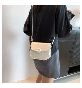 Detail shot of a minimalist white leather saddle bag with an elegant buckle on a model