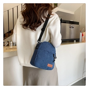 Detail shot of the blue corduroy crossbody bag texture and logo tag on model