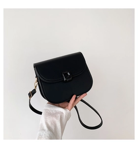 Detail of black leather saddle bag featuring a smooth flap and gold metal hook hardware