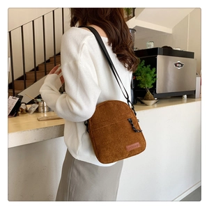 Detail of caramel corduroy crossbody bag featuring front zipper and brand tag detail