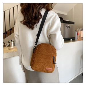 Close-up of brown corduroy crossbody bag with adjustable strap and logo detail