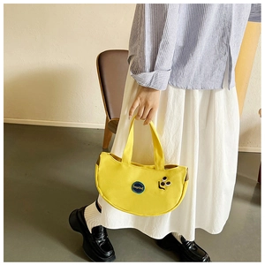 Close-up of yellow crescent canvas tote bag with cute smile embroidery and circular logo