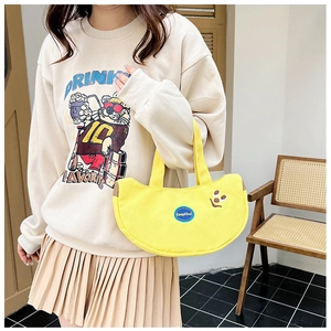 Model holding a yellow crescent canvas bag with smile embroidery in a cozy interior