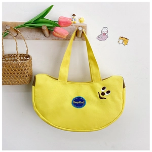 Detail of yellow canvas tote bag with KeepKind embroidery and a small black smiley face