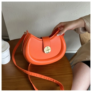 Top view of bright orange crescent bag with golden clasp on a wooden table