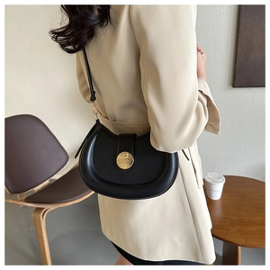 Side view of black crescent saddle bag with gold metal buckle on a model in city setting