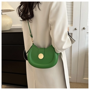 Detailed view of green crescent shoulder bag with large circular golden metal buckle closure