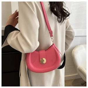 Pink crescent shoulder bag with large gold buckle worn over a beige coat