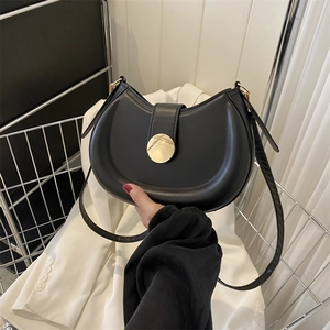 Detail of a black crescent moon bag with a gold circular magnetic clasp and smooth leather