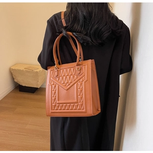 Close-up of brown quilted faux leather tote bag with elegant black fur ball charm detail