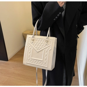 Detail of white square tote bag featuring geometric quilted texture and gold hardware