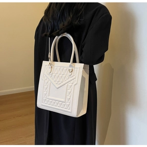 Detailed close-up of white tote bag featuring geometric embossed patterns and gold hardware