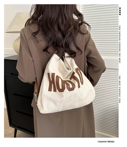 Detail of cream canvas tote bag with brown leather letter patch and shoulder strap