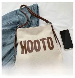 Detail of off-white canvas tote bag with brown leather HOOTO lettering and slim straps