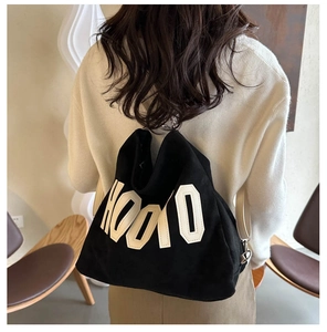 Detail of black canvas tote bag with HOOLO embroidery shown on a model in a cozy room