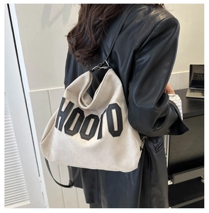 Detail of light beige canvas tote bag with black HOOTO lettering on model in black suit