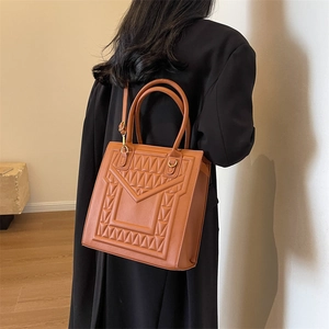 Brown box tote bag with geometric embossed pattern and gold hardware on black coat
