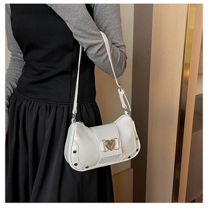 Detail of white glossy baguette bag featuring a gold heart clasp and silver studs decoration