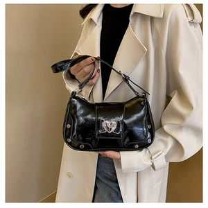 Detail of black patent leather shoulder bag with silver heart buckle and metal rivets