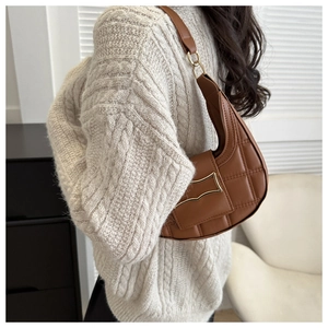 Close-up of brown quilted crescent bag featuring a unique wave-shaped golden metal clasp