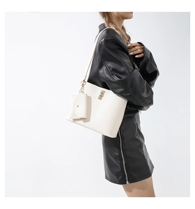 Detail of cream leather tote bag with gold buckle on a model in a black leather jacket