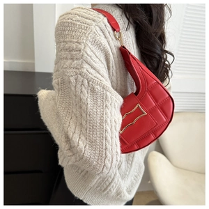Detail of red quilted crescent shoulder bag with gold clasp worn over a beige sweater