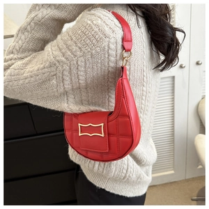 Detail of red quilted crescent shoulder bag featuring gold buckle and matte leather texture