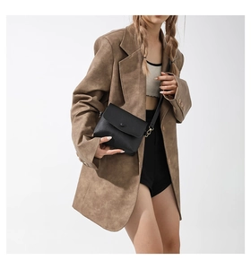 Classic black crossbody bag with matte texture and circular buckle on brown blazer