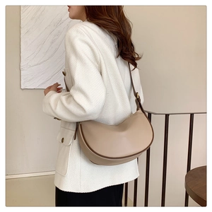 Side view of minimalist off-white half-moon shoulder bag with brown edges on a model