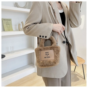 Gros plan d'un sac seau en peluche marron avec écusson en cuir et détails en métal