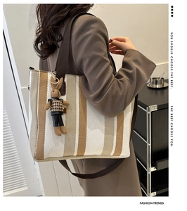 Detail of striped canvas tote bag featuring brown shoulder strap and plush rabbit charm