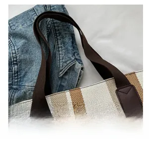 Detail of striped canvas tote bag with reinforced brown handles and leather accents