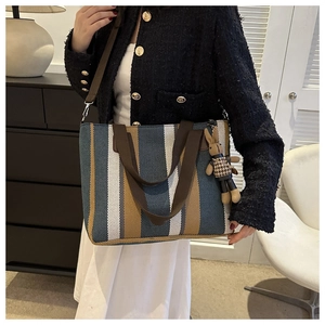 Vertical striped canvas tote bag detail with brown straps and cute rabbit charm pendant