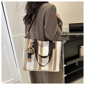 Detailed view of a striped canvas tote bag with a cute rabbit keychain in an office setting