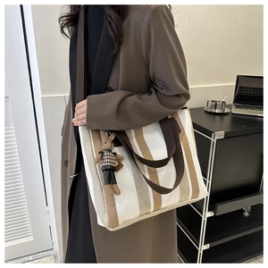 Detailed side view of striped canvas tote bag with bunny charm on model in professional setting