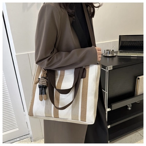 Detail view of striped canvas tote bag with textured weaving and plush bear charm