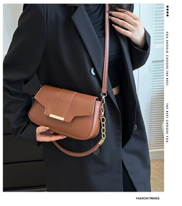 Detail of caramel brown leather handbag with gold metal bar and adjustable chain strap