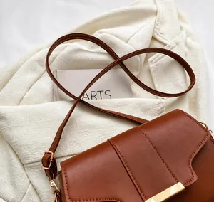 Detail shot of brown leather shoulder bag featuring a gold metal bar and adjustable strap