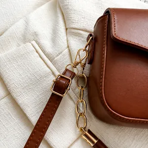 Detail of high-quality brown leather texture and shiny gold hardware on a crossbody bag
