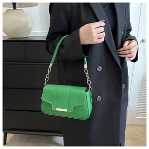 Detail of bright green shoulder bag with gold chain strap and metallic flap trim