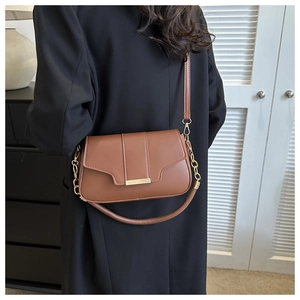 Detail of a brown rectangular crossbody bag with gold buckle on a black coat
