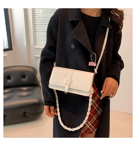 Detalle de bolso bandolera crema con correa tejida y hebilla cuadrada en modelo