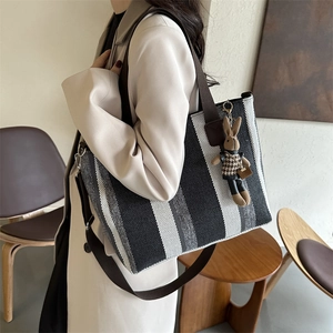 Large striped tote bag with rabbit charm and wide shoulder strap shown on a model