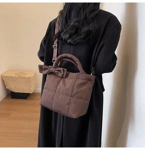Detail of dark brown quilted tote bag with large decorative bow on model in black coat